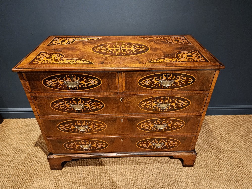 A George III period walnut chest of drawers featuring decorative oval marquetry inlays across four drawer fronts and brass handles, resting on bracket feet. View II