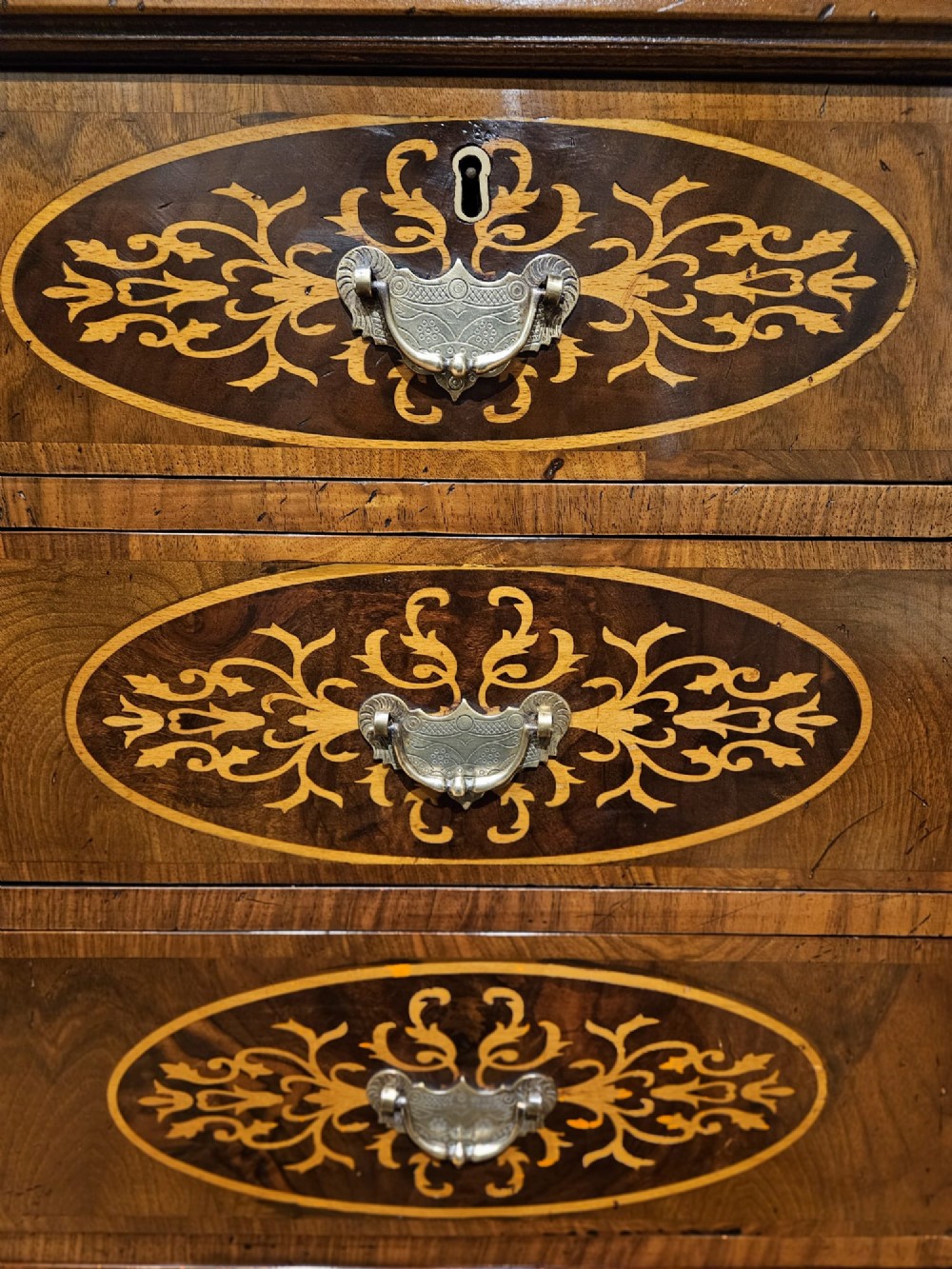 A George III period walnut chest of drawers featuring decorative oval marquetry inlays across four drawer fronts and brass handles, resting on bracket feet. View III