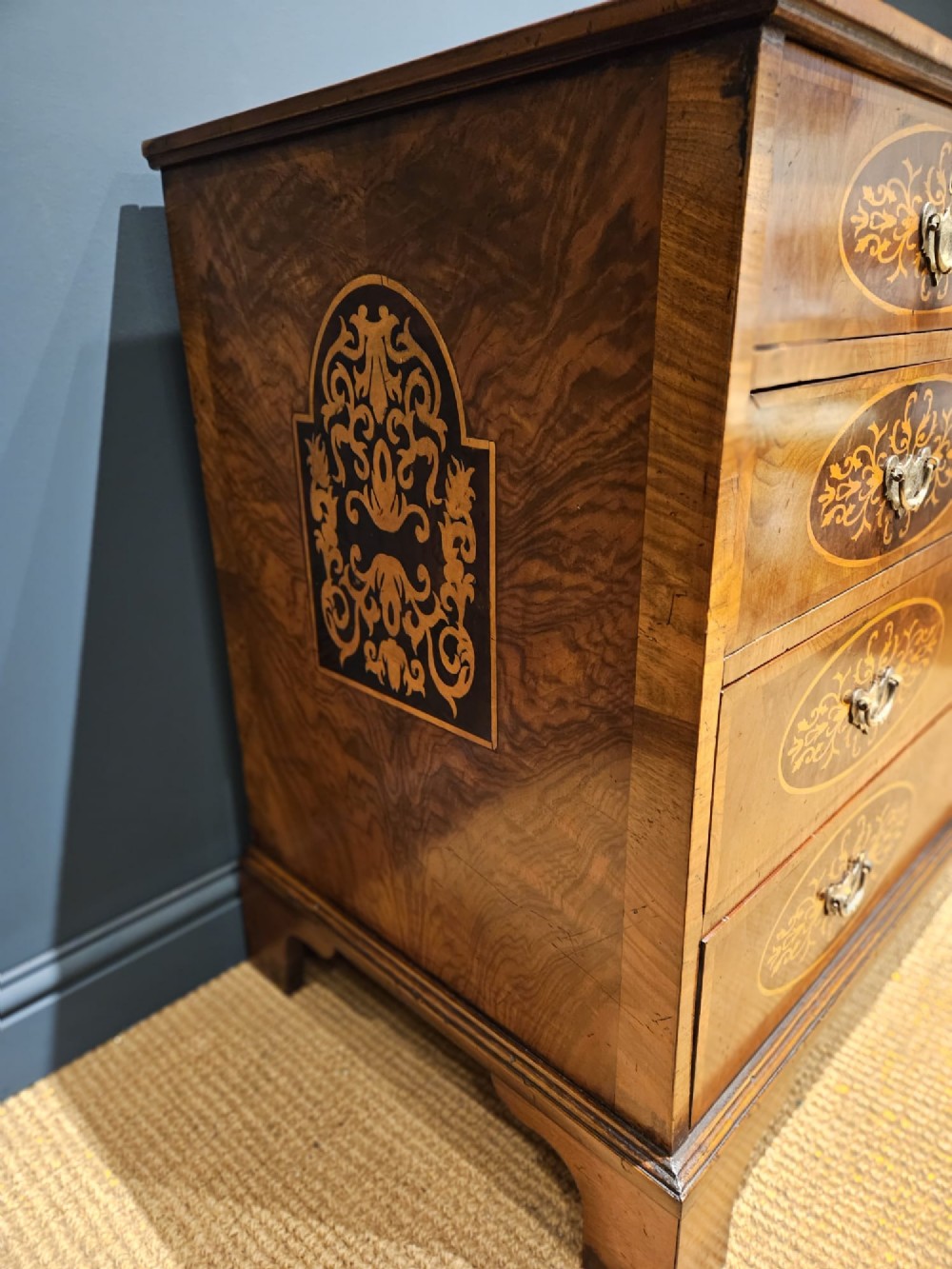 A George III period walnut chest of drawers featuring decorative oval marquetry inlays across four drawer fronts and brass handles, resting on bracket feet. View IV