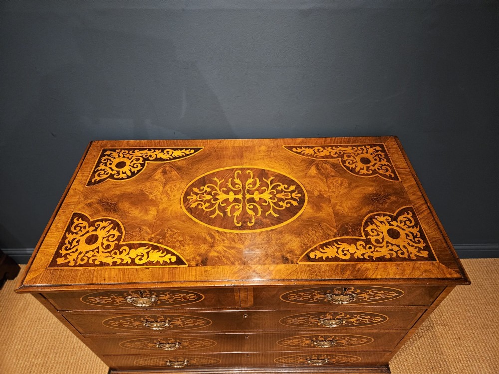 A George III period walnut chest of drawers featuring decorative oval marquetry inlays across four drawer fronts and brass handles, resting on bracket feet. View V