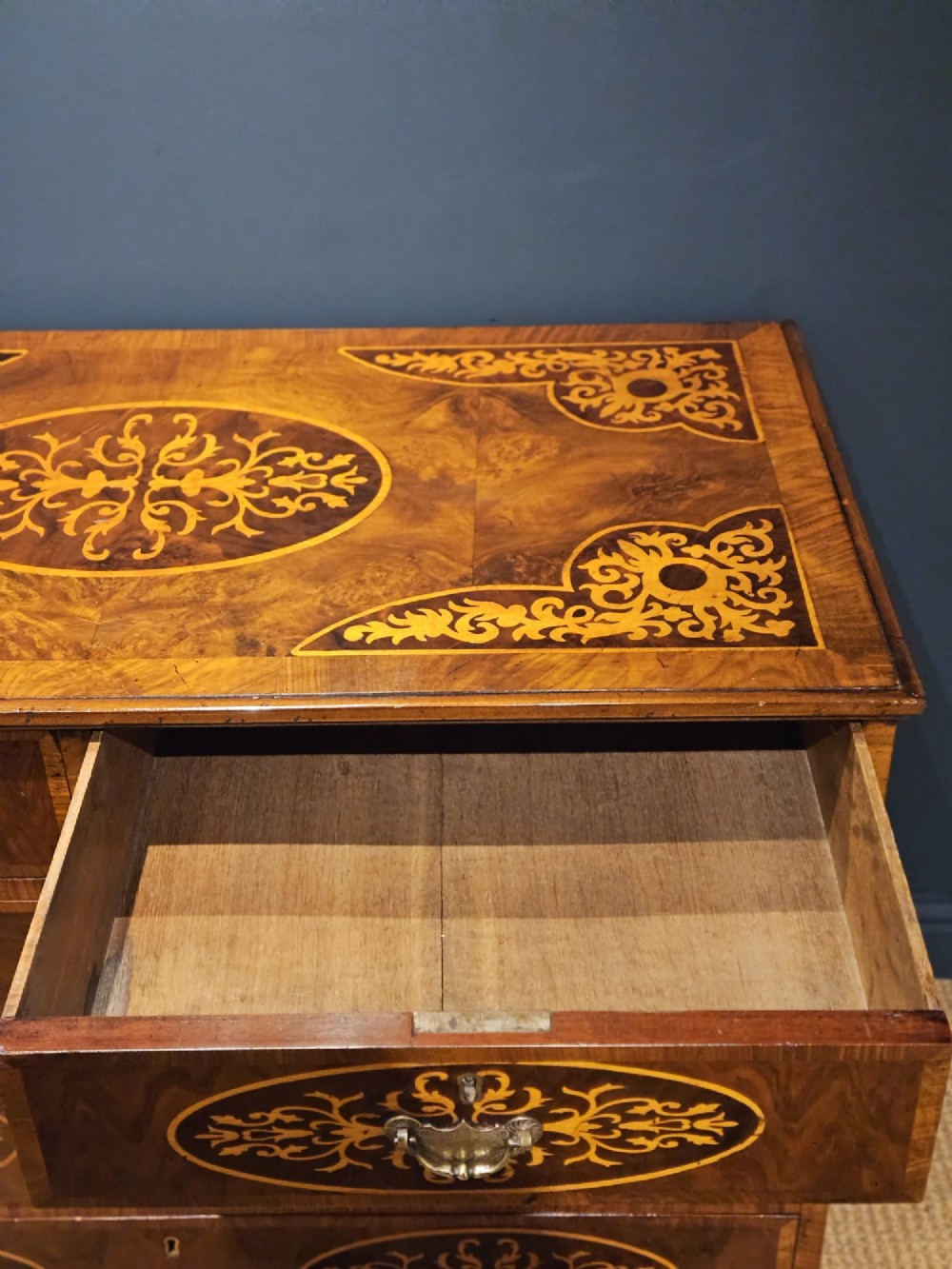 A George III period walnut chest of drawers featuring decorative oval marquetry inlays across four drawer fronts and brass handles, resting on bracket feet. View VI