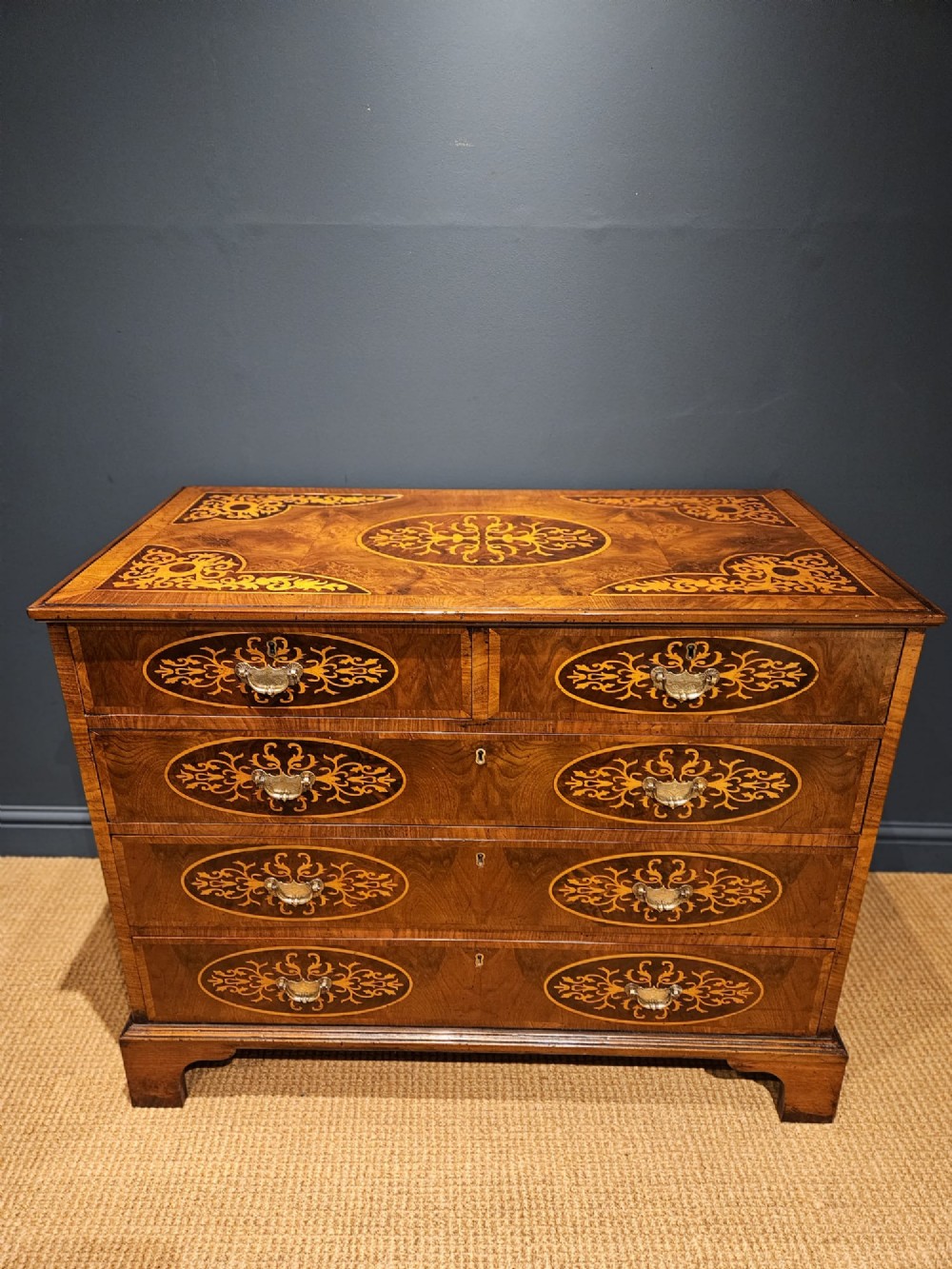 A George III period walnut chest of drawers featuring decorative oval marquetry inlays across four drawer fronts and brass handles, resting on bracket feet. View VIII