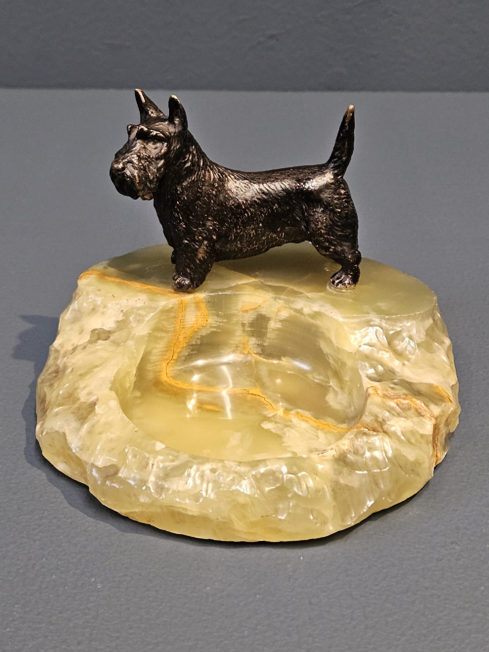 A cold painted bronze Scottish Terrier figure standing on a carved pale green onyx dish with natural veining.