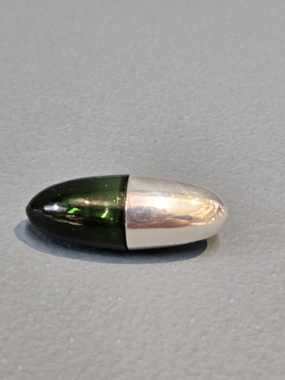 A Victorian torpedo-shaped scent bottle featuring a polished silver top half and a deep emerald green glass base.