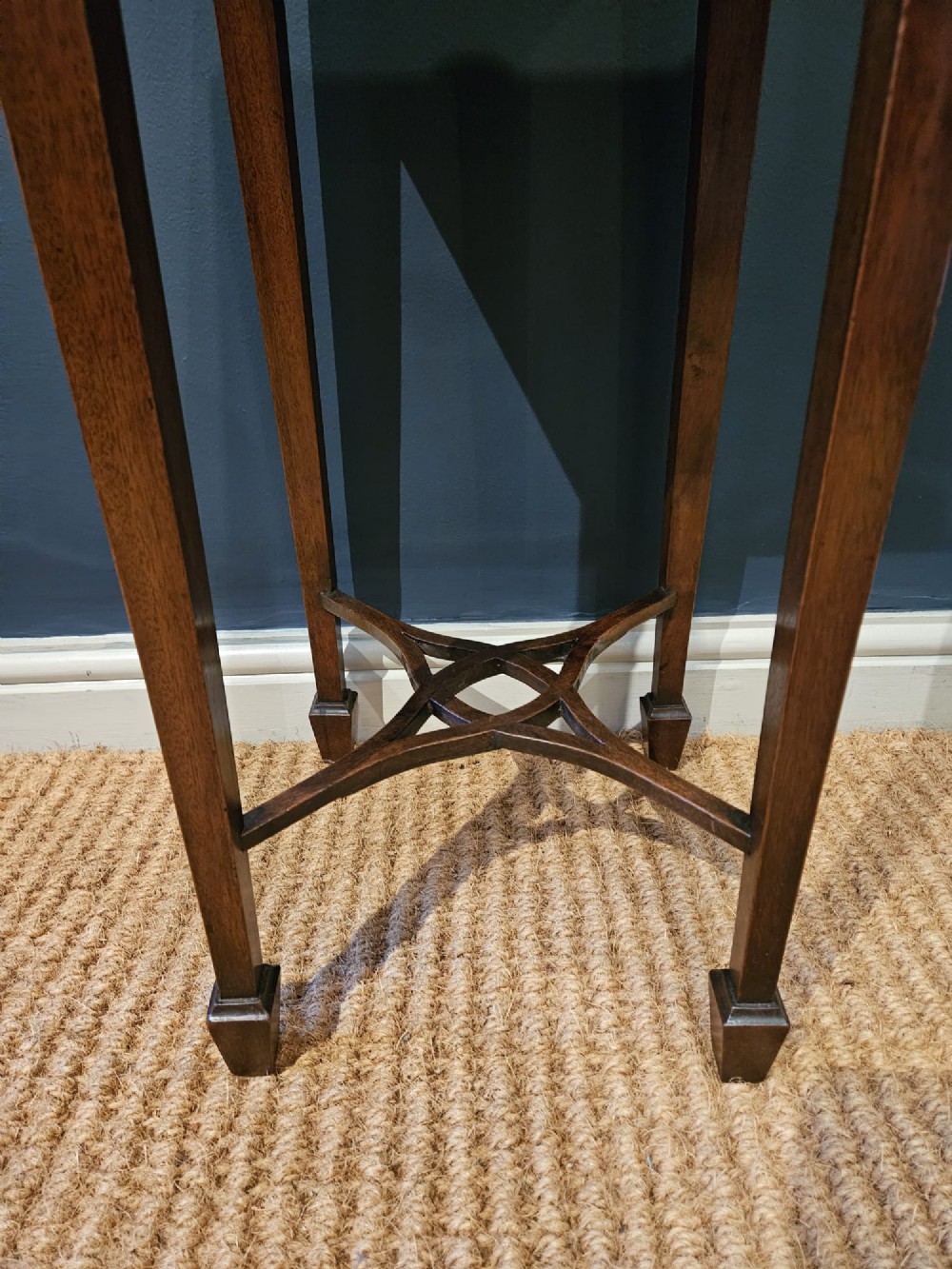 A tall Edwardian mahogany kettle stand featuring a scalloped gallery top, a small drawer with a brass pull, square tapered legs, and a crossed stretcher base. View VI