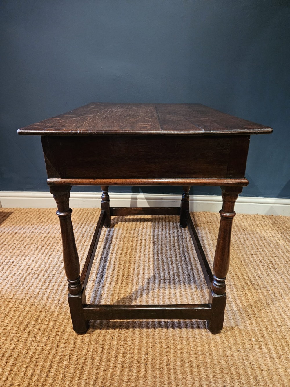 A dark oak George I side table featuring a single frieze drawer with brass drop handles and turned legs joined by stretchers. View II