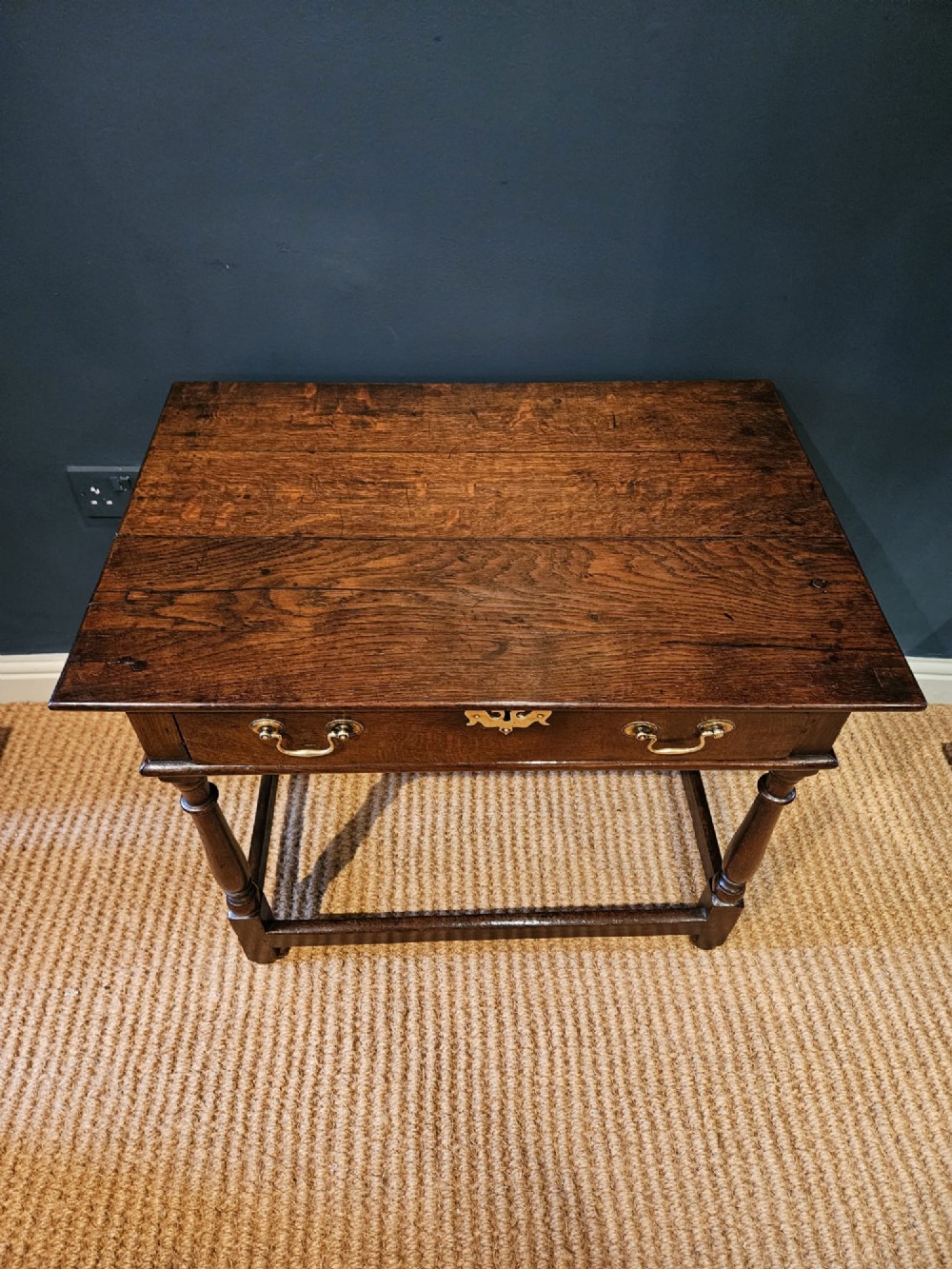 A dark oak George I side table featuring a single frieze drawer with brass drop handles and turned legs joined by stretchers. View VIII