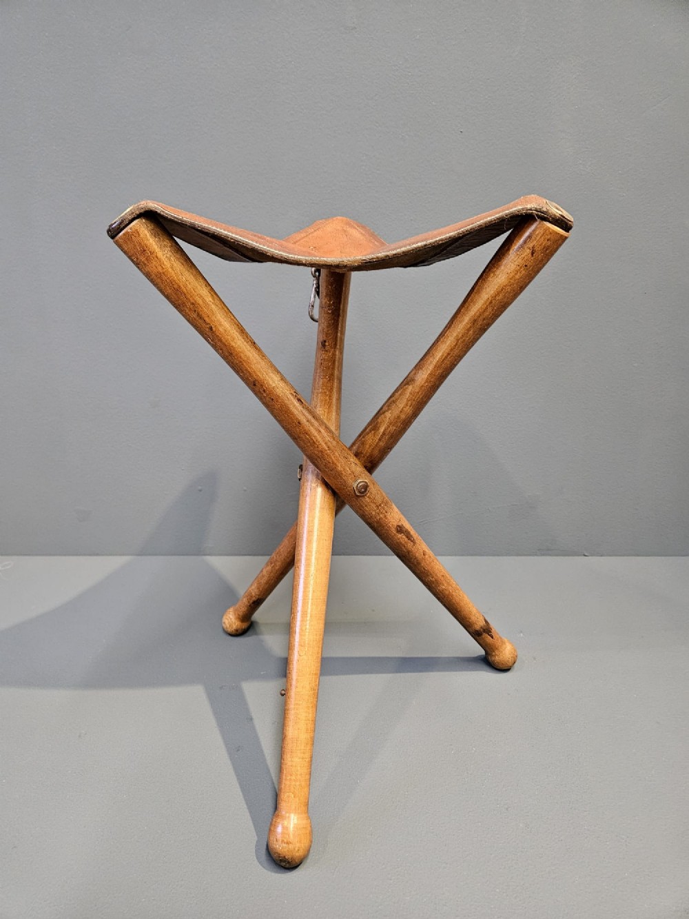 An Arts and Crafts period folding tripod campaign stool with three turned wooden legs and a stitched tan leather seat. View III