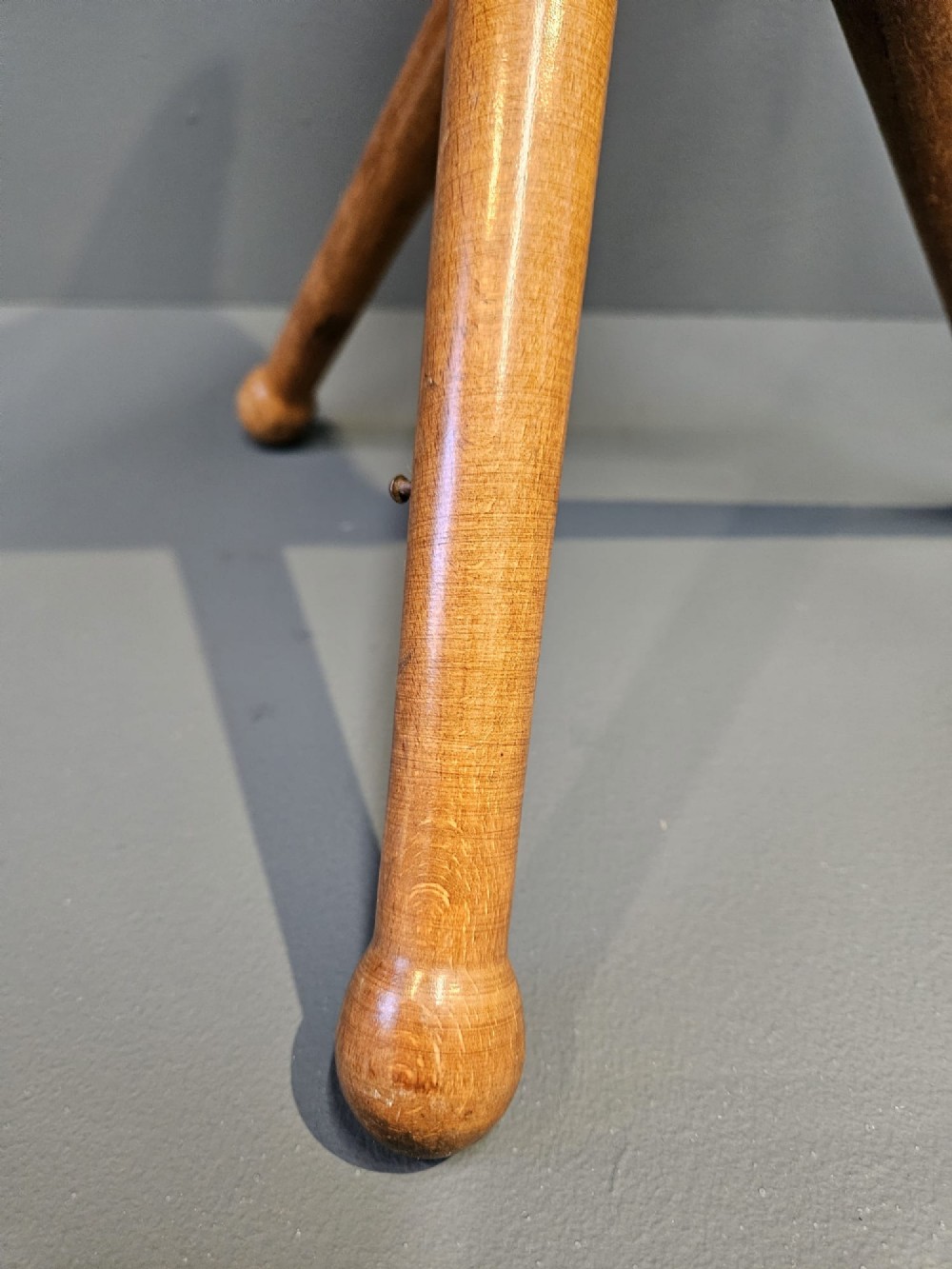 An Arts and Crafts period folding tripod campaign stool with three turned wooden legs and a stitched tan leather seat. View IV
