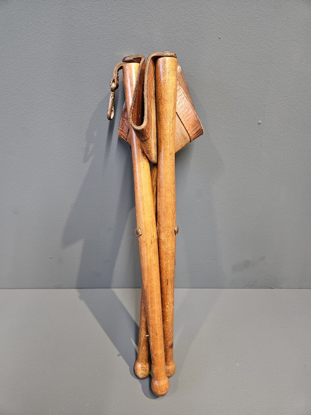An Arts and Crafts period folding tripod campaign stool with three turned wooden legs and a stitched tan leather seat. View V