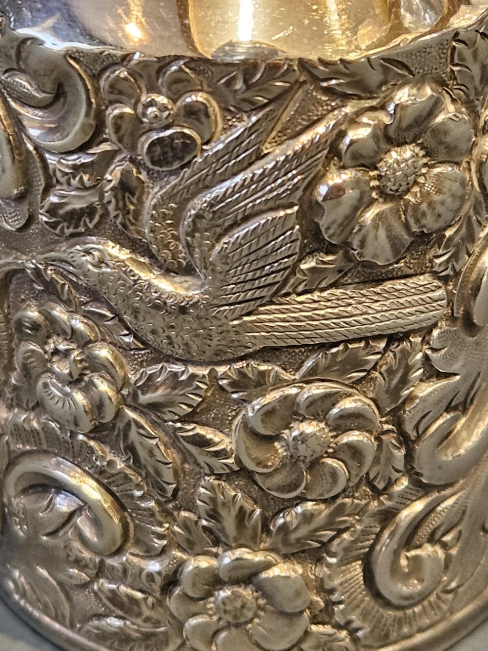 A cylindrical Victorian sterling silver cologne bottle with detailed chased floral scrollwork, bird motifs, and a matching screw cap. View VI