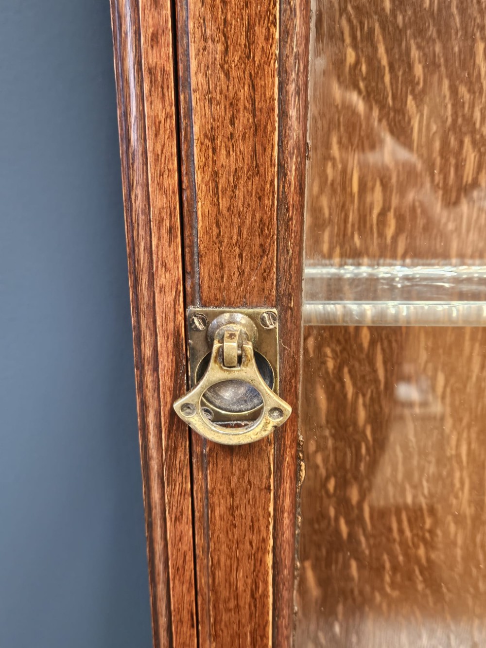 An Edwardian warm brown oak wall-mounted display cabinet with a single glass door featuring gold lettering that reads OPTICIAN over internal glass shelves. View V