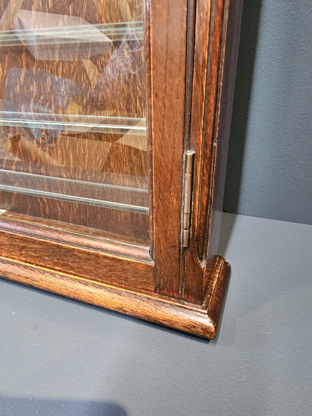 An Edwardian warm brown oak wall-mounted display cabinet with a single glass door featuring gold lettering that reads OPTICIAN over internal glass shelves. View VII