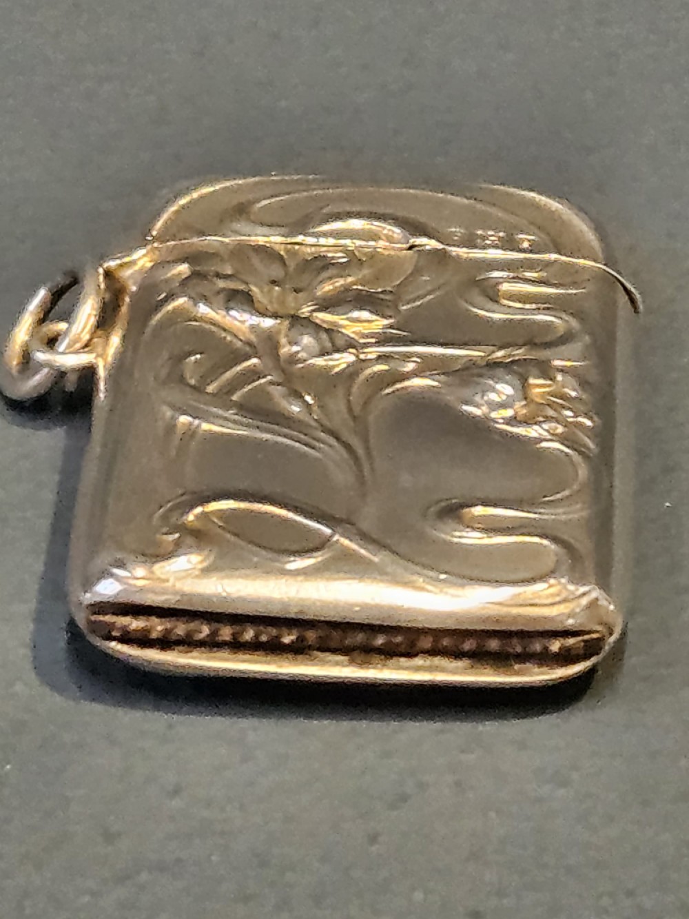 An Art Nouveau sterling silver vesta case featuring embossed floral motifs and whiplash scroll decoration with visible British hallmarks and a side suspension ring. View III