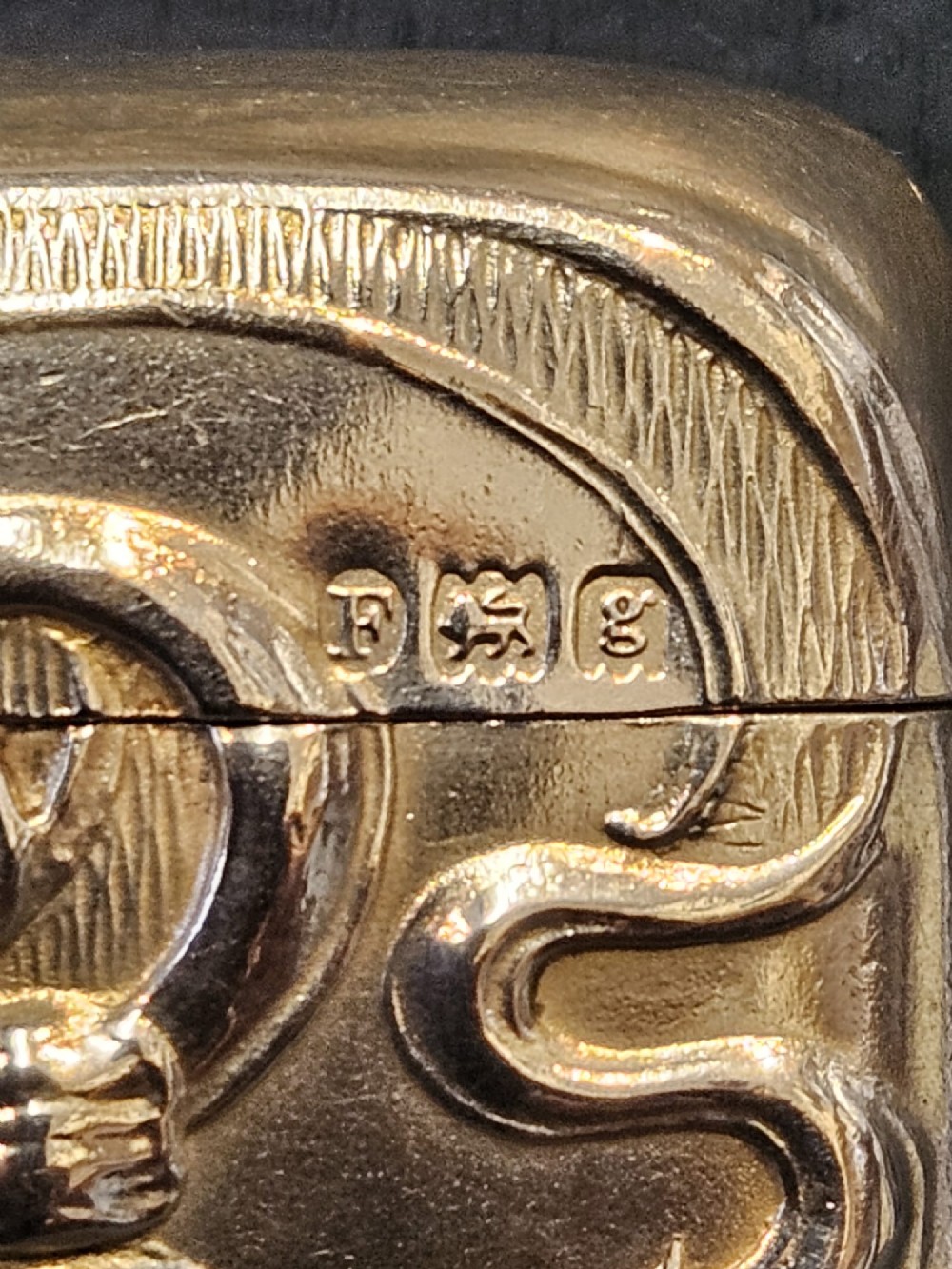 An Art Nouveau sterling silver vesta case featuring embossed floral motifs and whiplash scroll decoration with visible British hallmarks and a side suspension ring. View IV