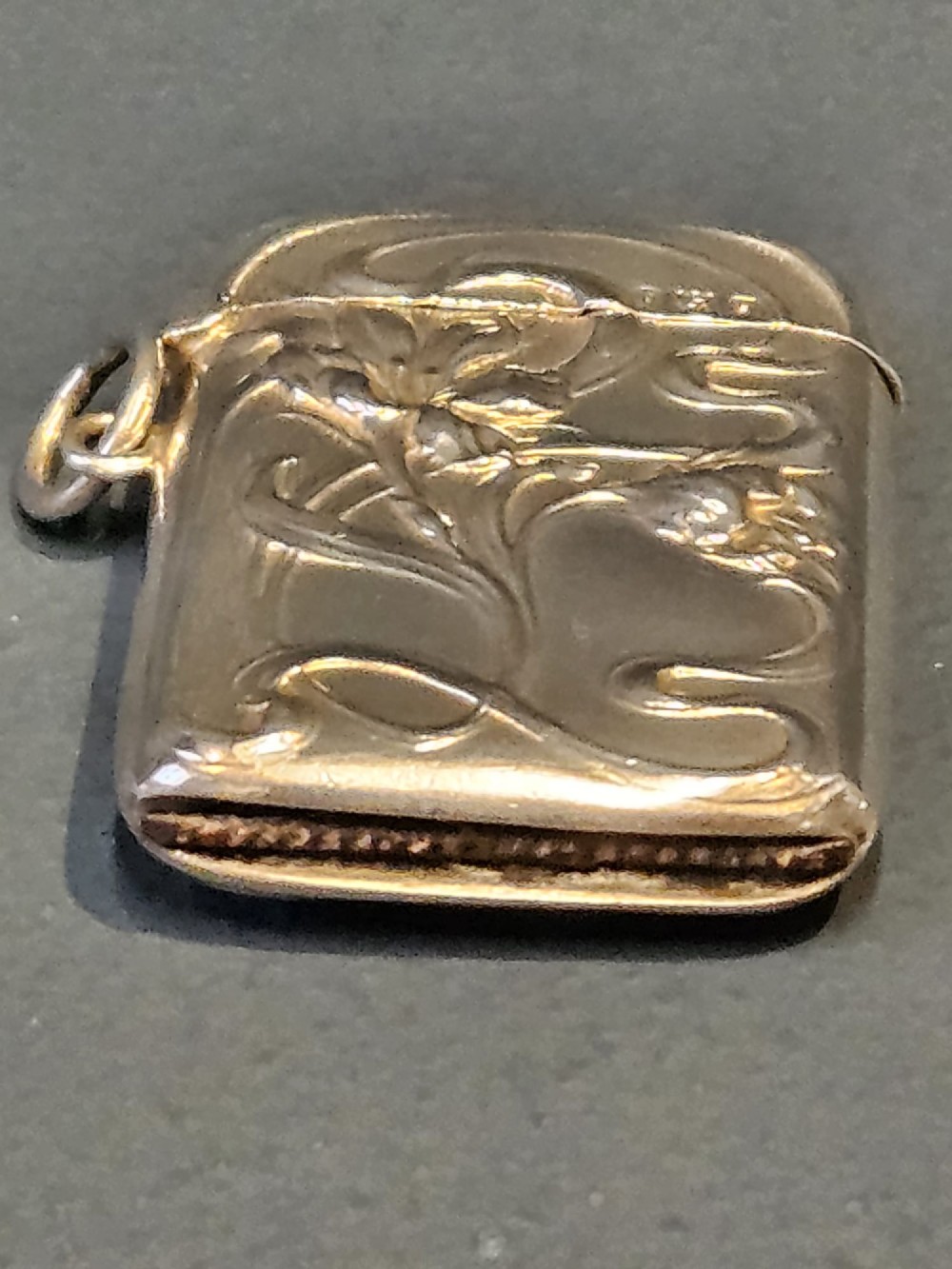 An Art Nouveau sterling silver vesta case featuring embossed floral motifs and whiplash scroll decoration with visible British hallmarks and a side suspension ring. View V