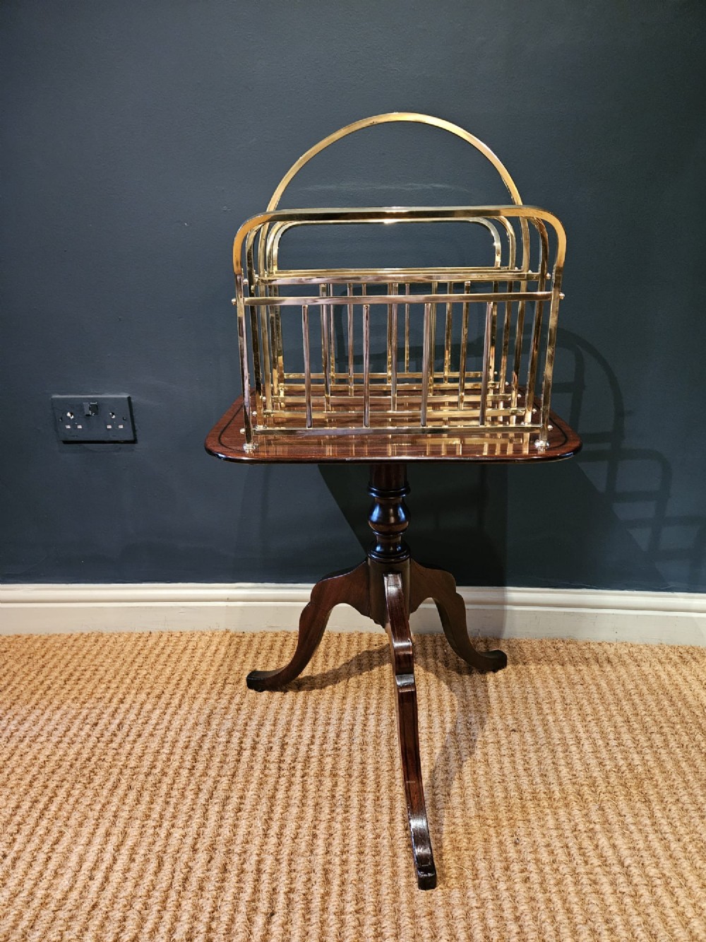 A Victorian brass magazine rack with vertical partitioned dividers mounted atop a polished mahogany tripod table base.