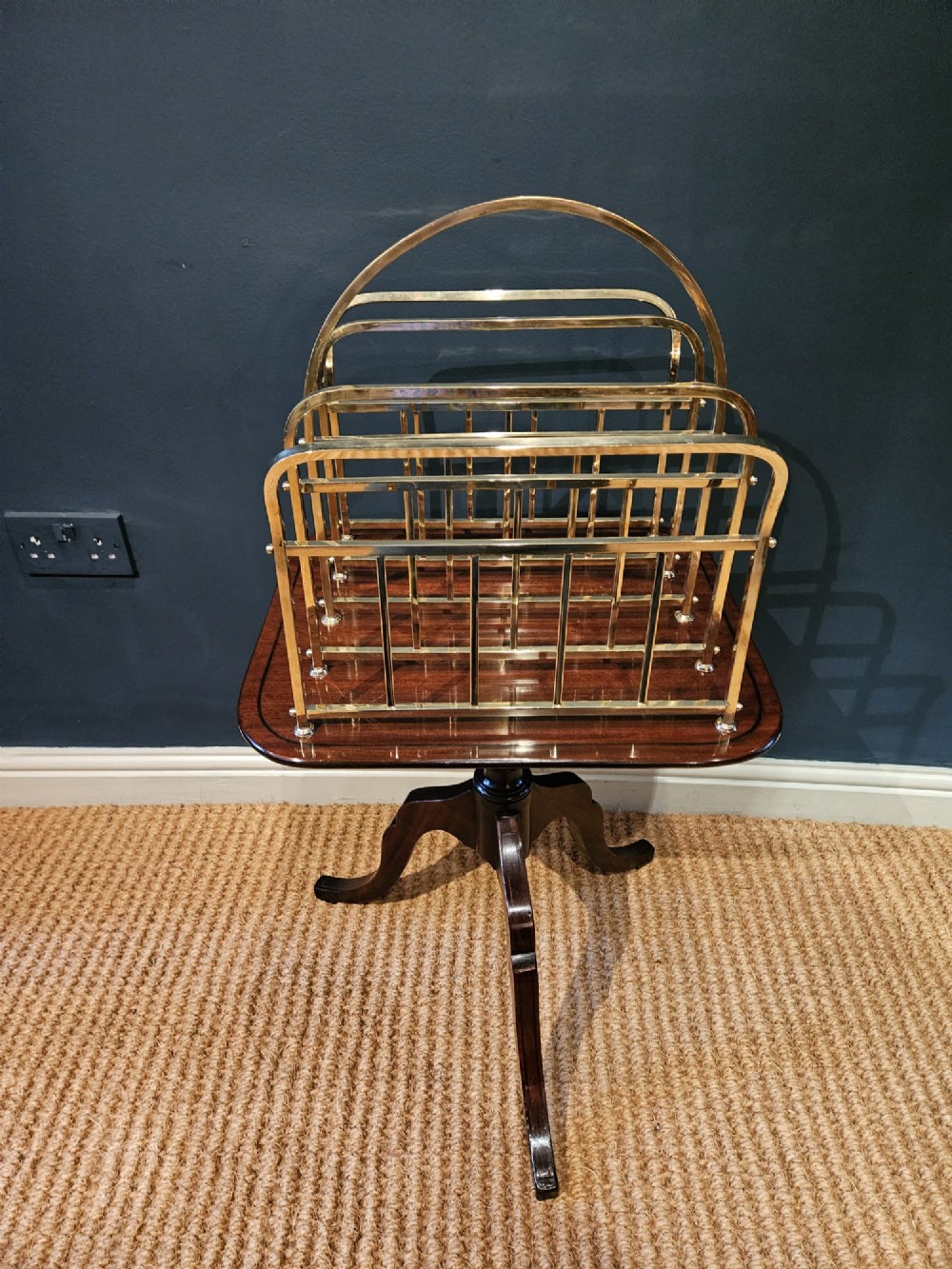 A Victorian brass magazine rack with vertical partitioned dividers mounted atop a polished mahogany tripod table base. View II