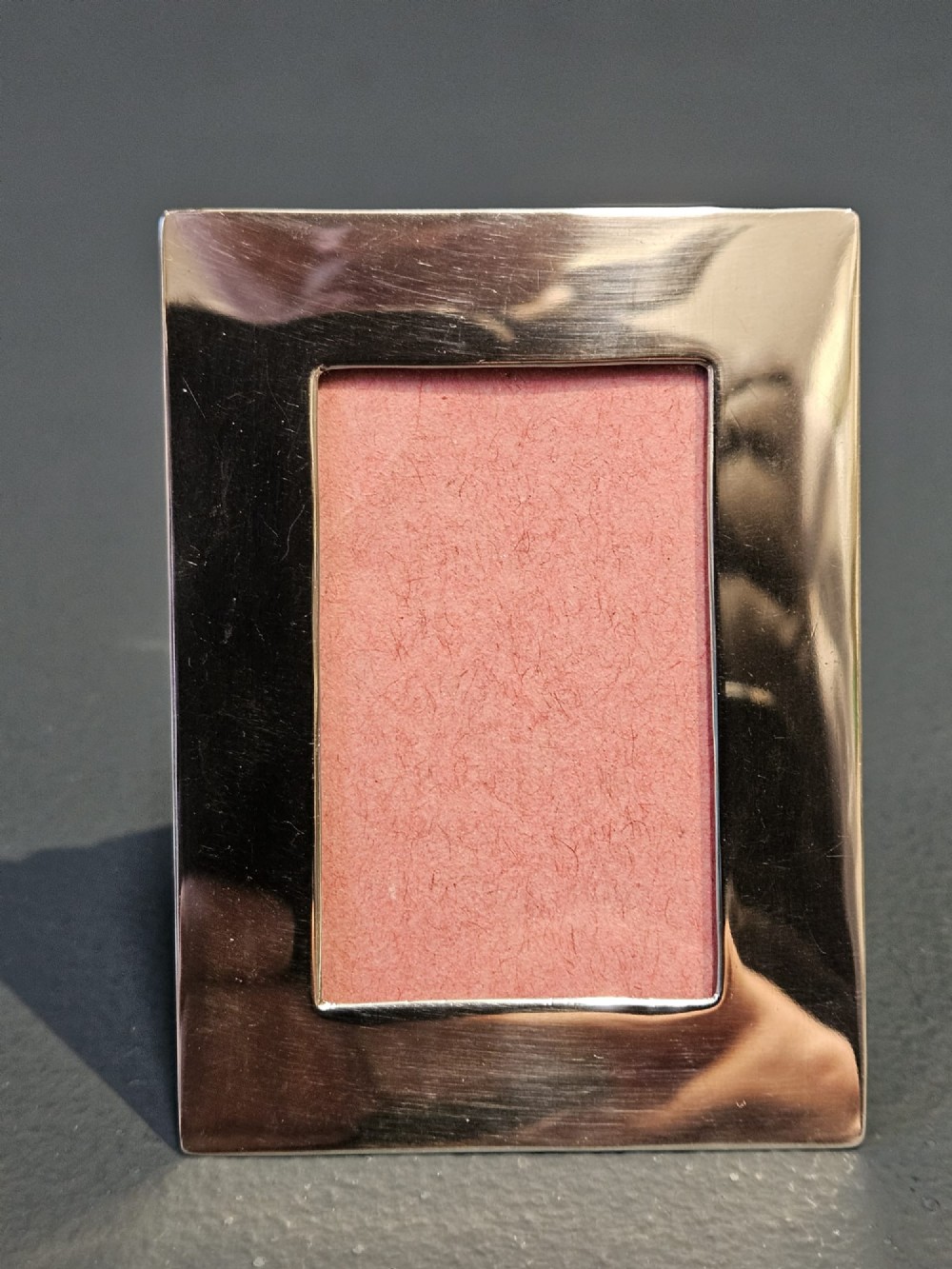 A small rectangular Edwardian polished silver photo frame featuring a plain border and a pink textured insert.