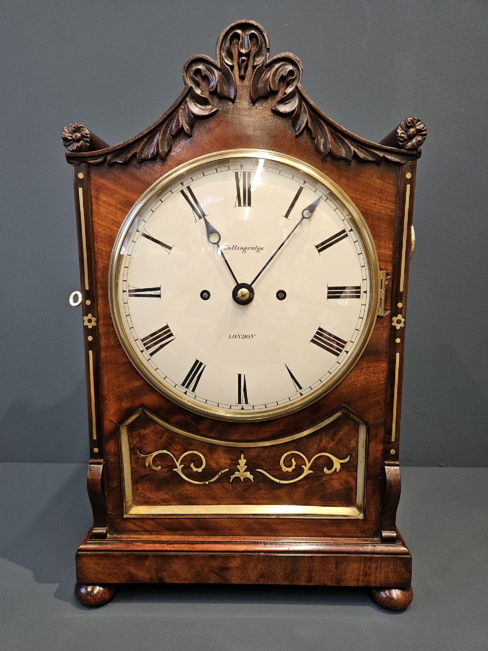A William IV carved mahogany bracket clock featuring brass inlay decoration, a circular dial with Roman numerals, and a matching wall bracket. View III