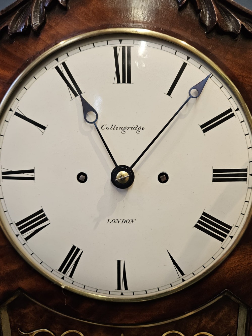 A William IV carved mahogany bracket clock featuring brass inlay decoration, a circular dial with Roman numerals, and a matching wall bracket. View IV