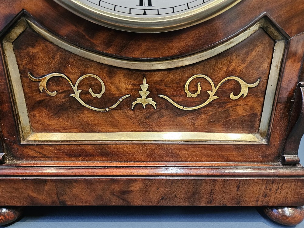 A William IV carved mahogany bracket clock featuring brass inlay decoration, a circular dial with Roman numerals, and a matching wall bracket. View V