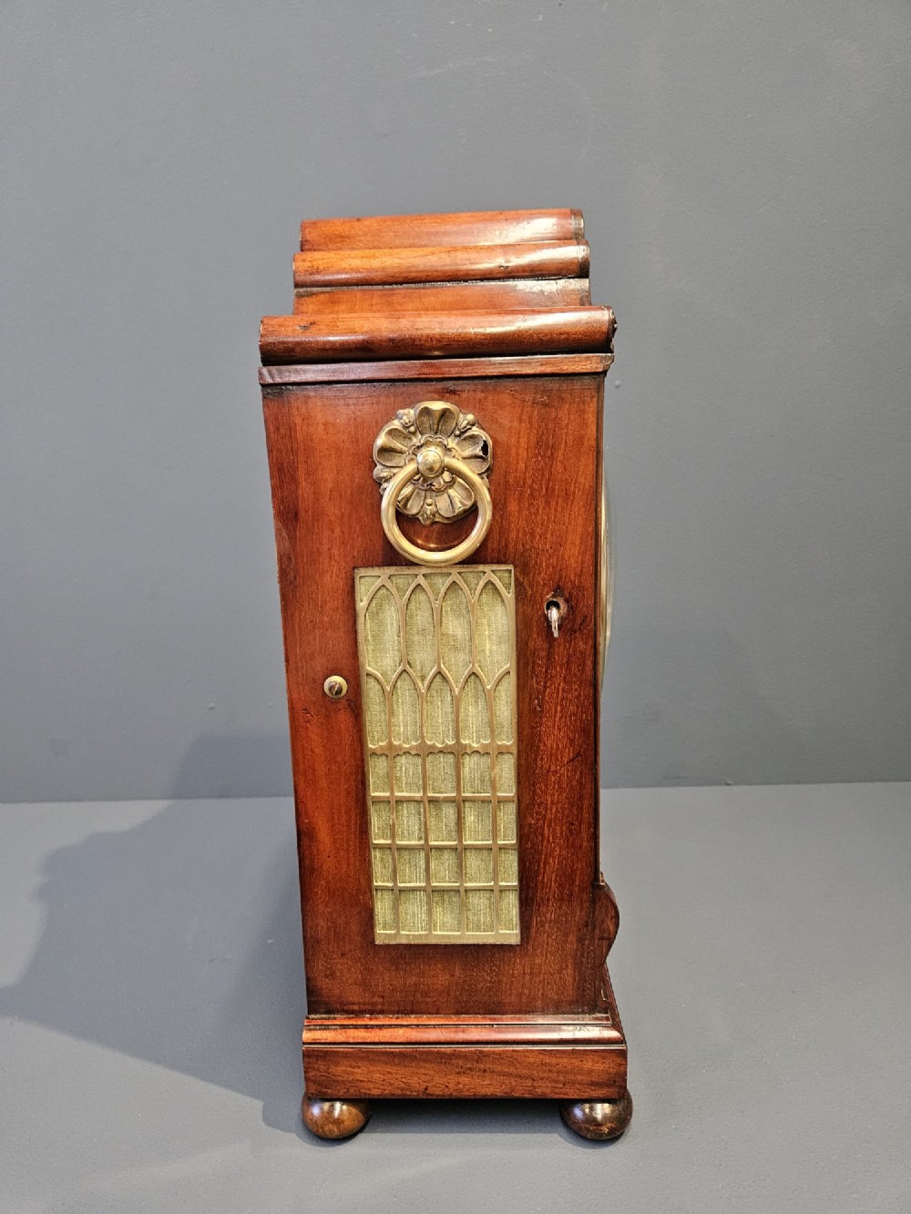 A William IV carved mahogany bracket clock featuring brass inlay decoration, a circular dial with Roman numerals, and a matching wall bracket. View VII