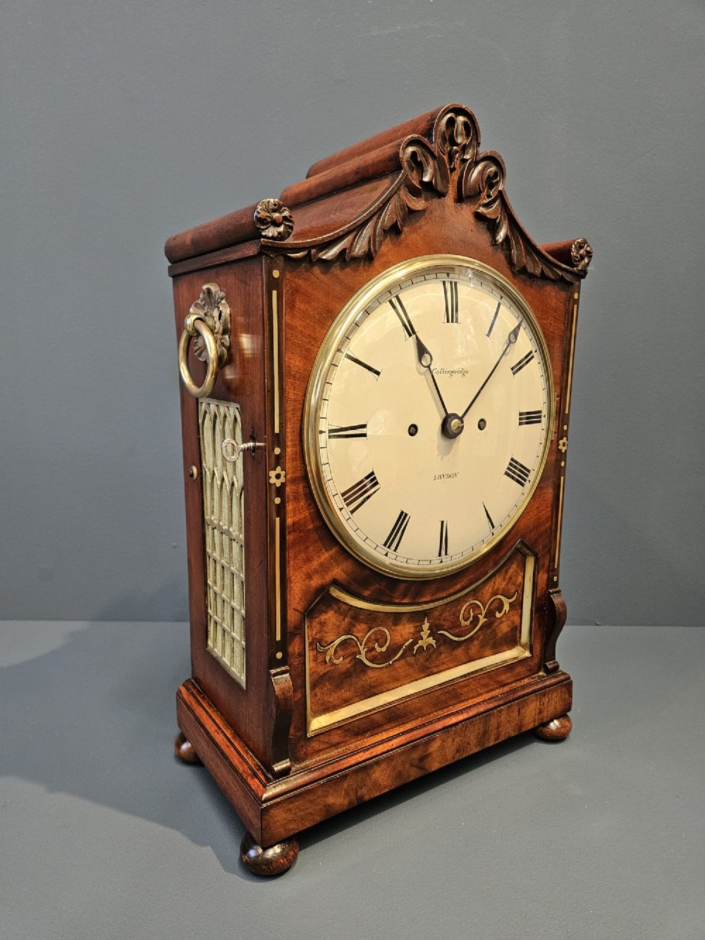 A William IV carved mahogany bracket clock featuring brass inlay decoration, a circular dial with Roman numerals, and a matching wall bracket. View IX