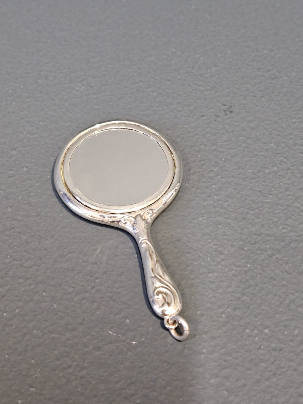An Edwardian Art Nouveau sterling silver flirting mirror featuring embossed relief floral lily decoration and a suspension ring. View II