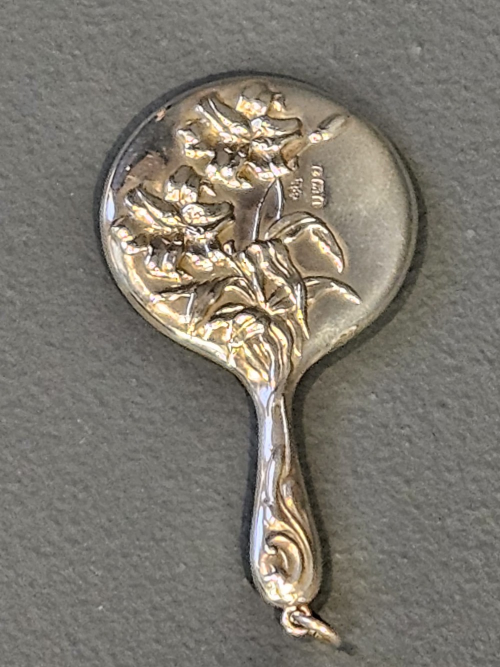 An Edwardian Art Nouveau sterling silver flirting mirror featuring embossed relief floral lily decoration and a suspension ring. View III