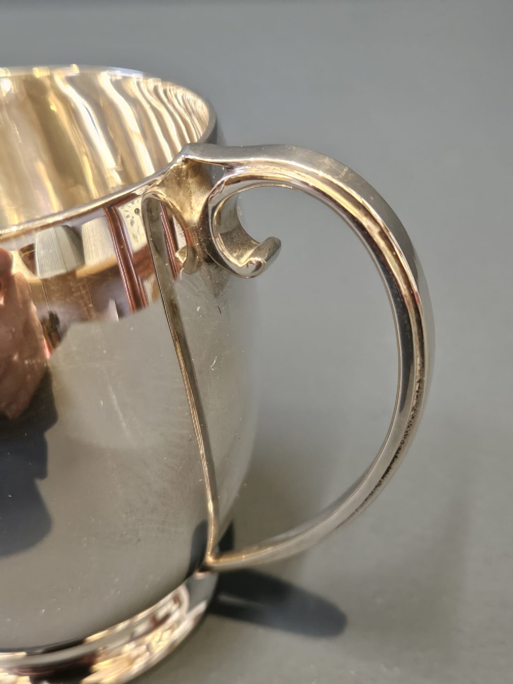 A polished silver mug featuring a bulbous body, a stepped base, and a scroll handle. View III