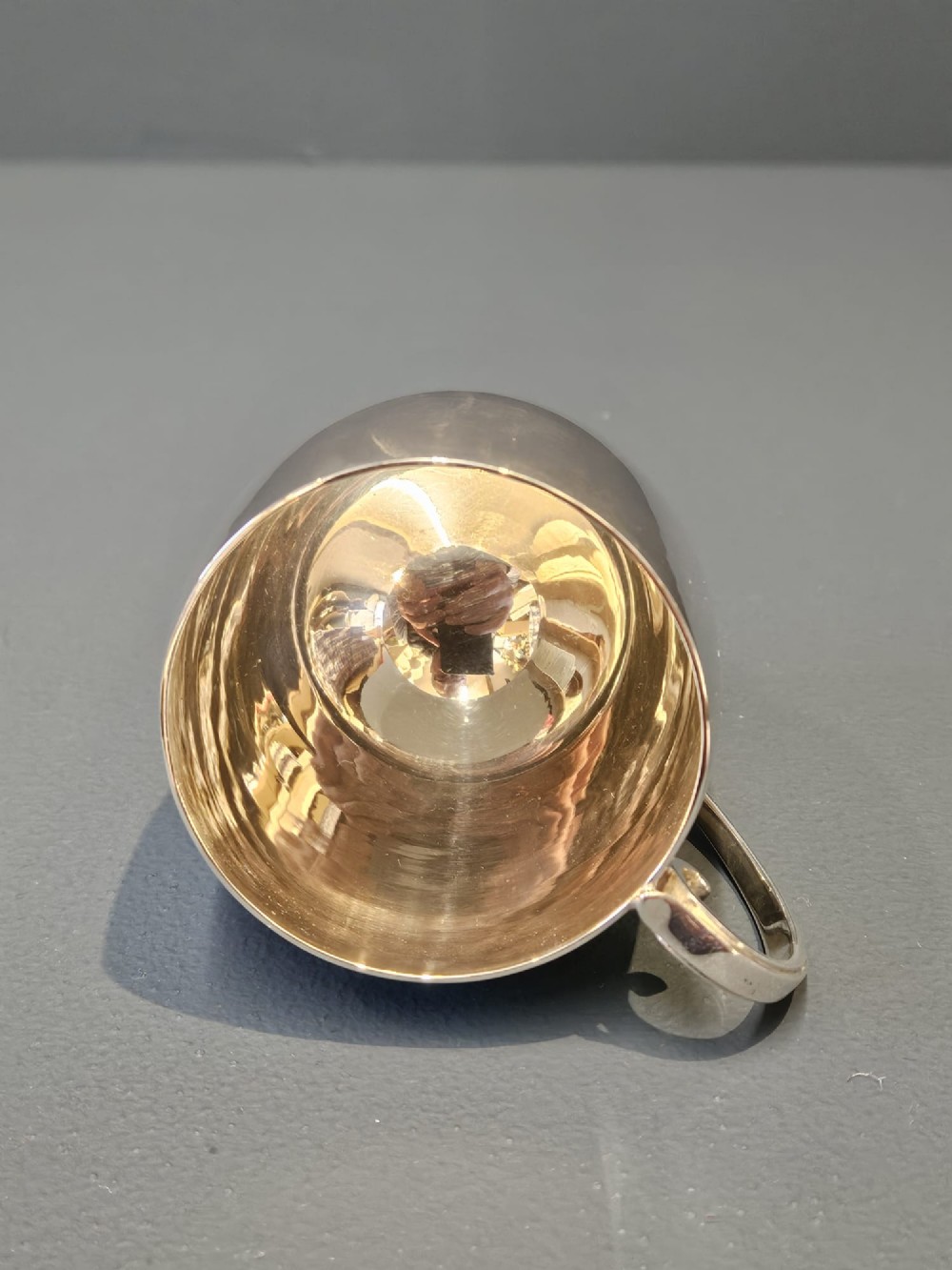 A polished silver mug featuring a bulbous body, a stepped base, and a scroll handle. View IV