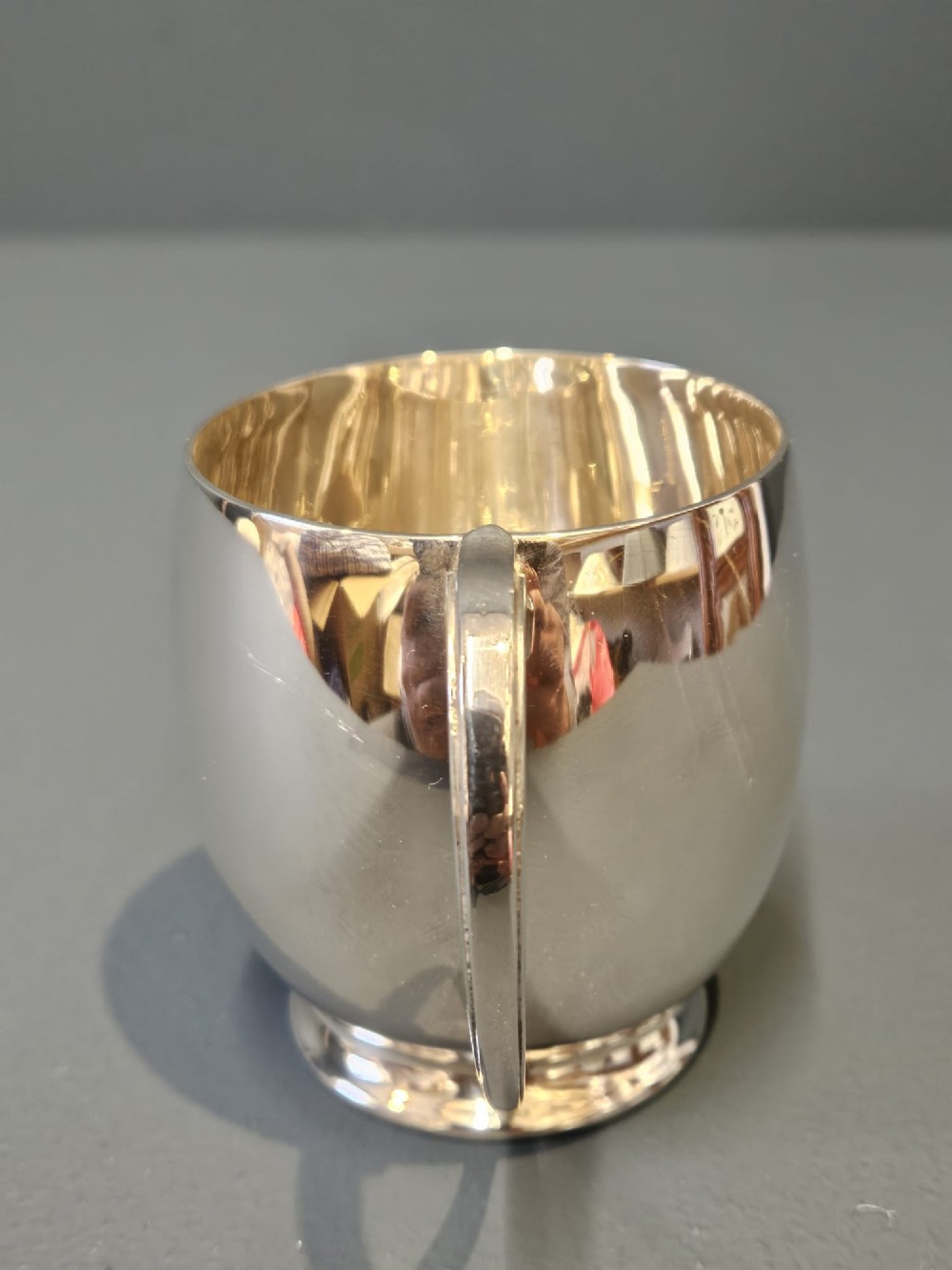 A polished silver mug featuring a bulbous body, a stepped base, and a scroll handle. View V