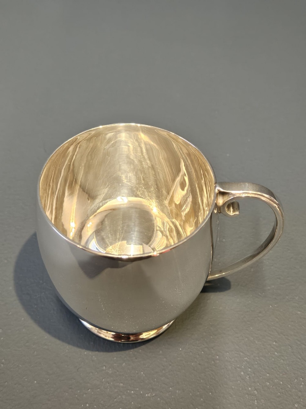 A polished silver mug featuring a bulbous body, a stepped base, and a scroll handle. View VII