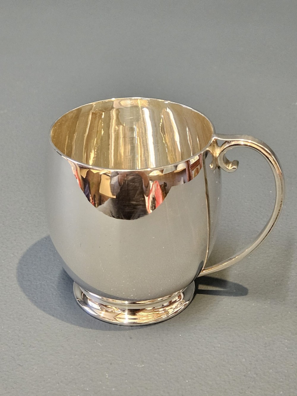 A polished silver mug featuring a bulbous body, a stepped base, and a scroll handle. View VIII