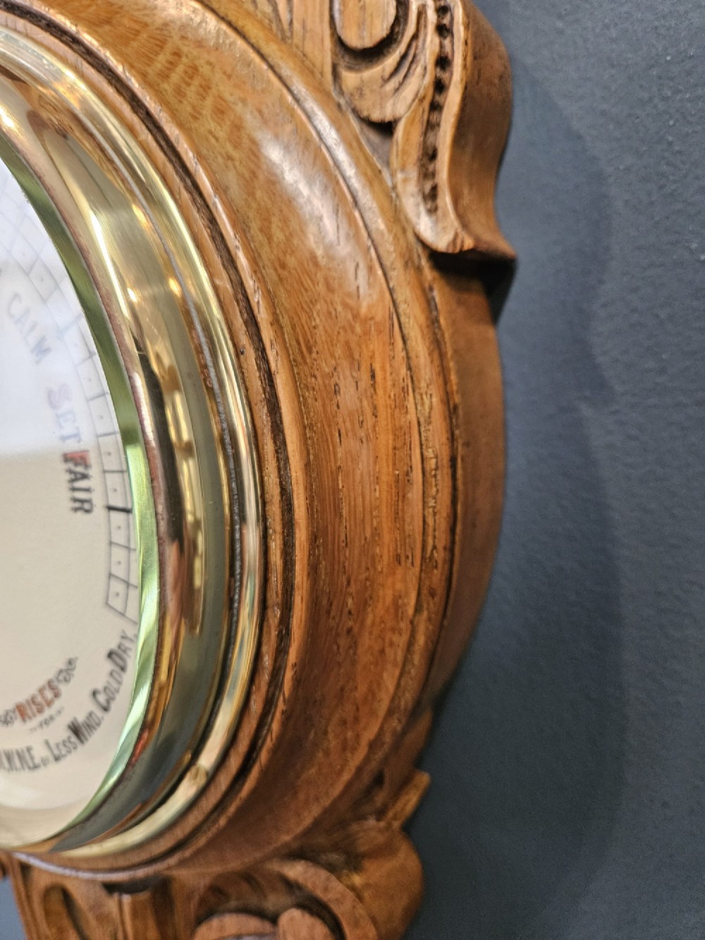 A carved Victorian golden oak banjo barometer with an integrated thermometer above a circular brass aneroid dial. View IV