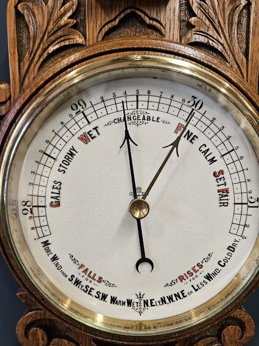 A carved Victorian golden oak banjo barometer with an integrated thermometer above a circular brass aneroid dial. View V