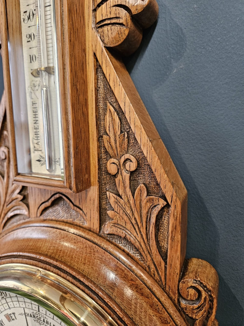 A carved Victorian golden oak banjo barometer with an integrated thermometer above a circular brass aneroid dial. View VI