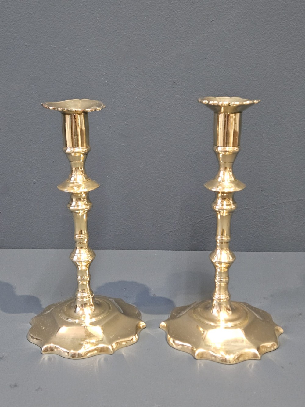 A pair of cast George II brass candlesticks featuring knopped baluster stems and lobed petal-shaped bases.