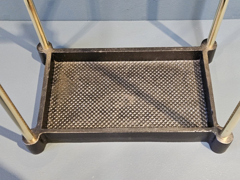 An Edwardian brass stick stand featuring four upright posts topped with urn finials, six upper compartments, and a textured black cast iron drip tray base. View III