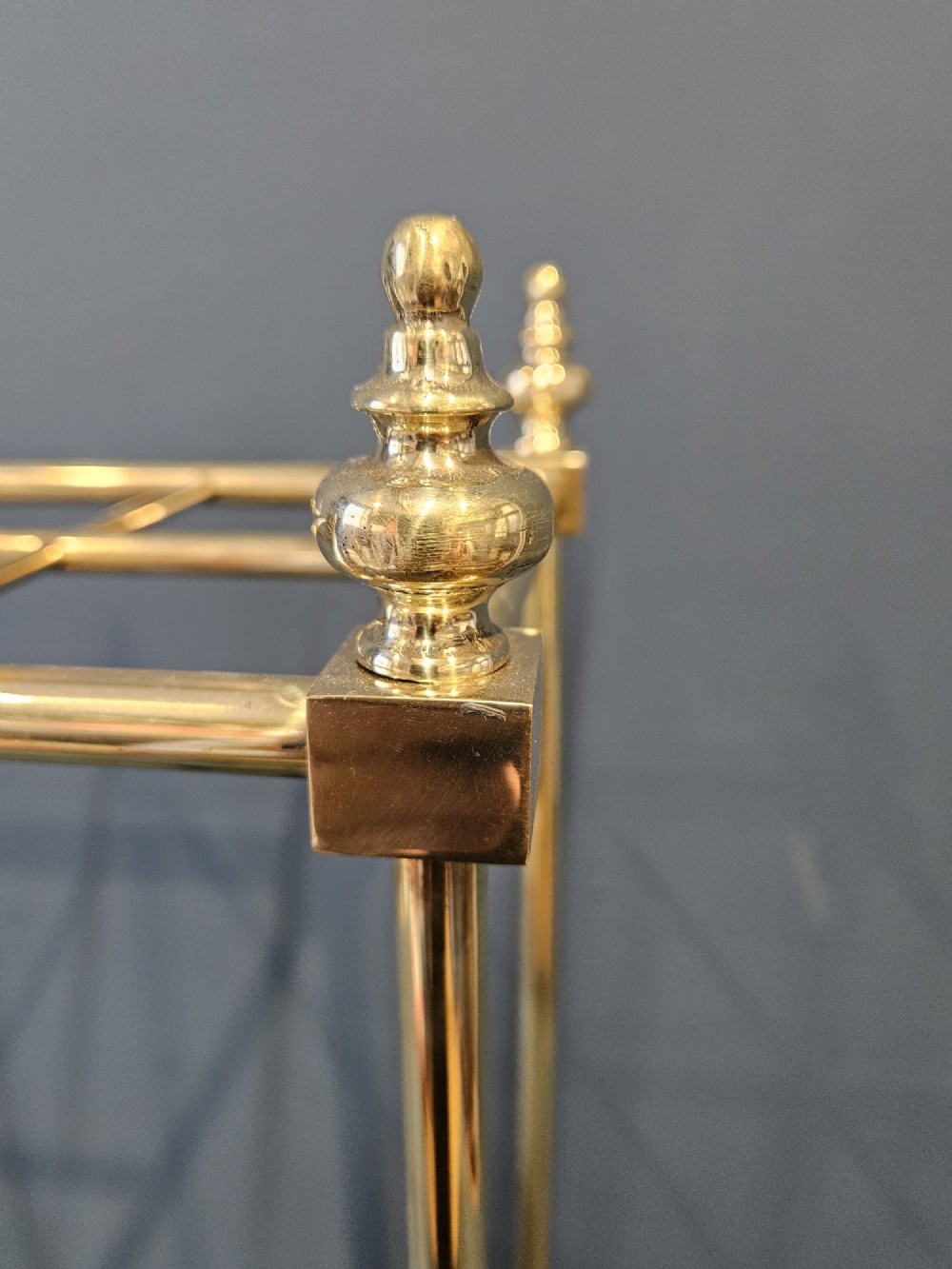 An Edwardian brass stick stand featuring four upright posts topped with urn finials, six upper compartments, and a textured black cast iron drip tray base. View V