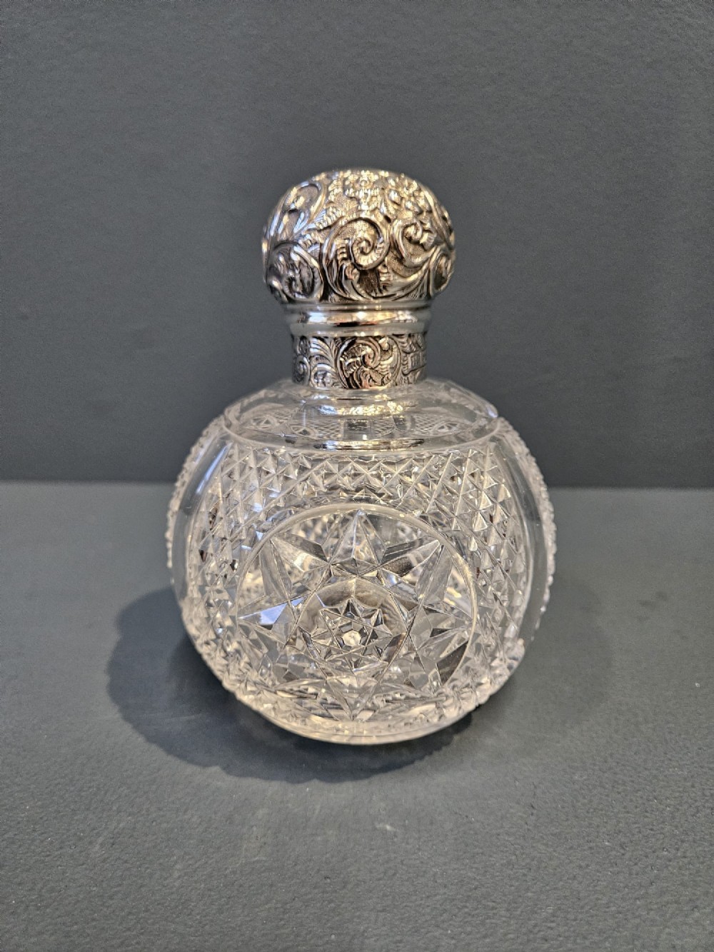 A late Victorian clear cut crystal scent bottle featuring a spherical body with a starburst pattern and an embossed silver cap.