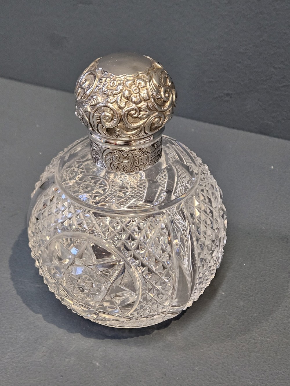 A late Victorian clear cut crystal scent bottle featuring a spherical body with a starburst pattern and an embossed silver cap. View III