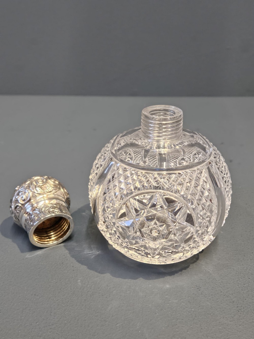 A late Victorian clear cut crystal scent bottle featuring a spherical body with a starburst pattern and an embossed silver cap. View V