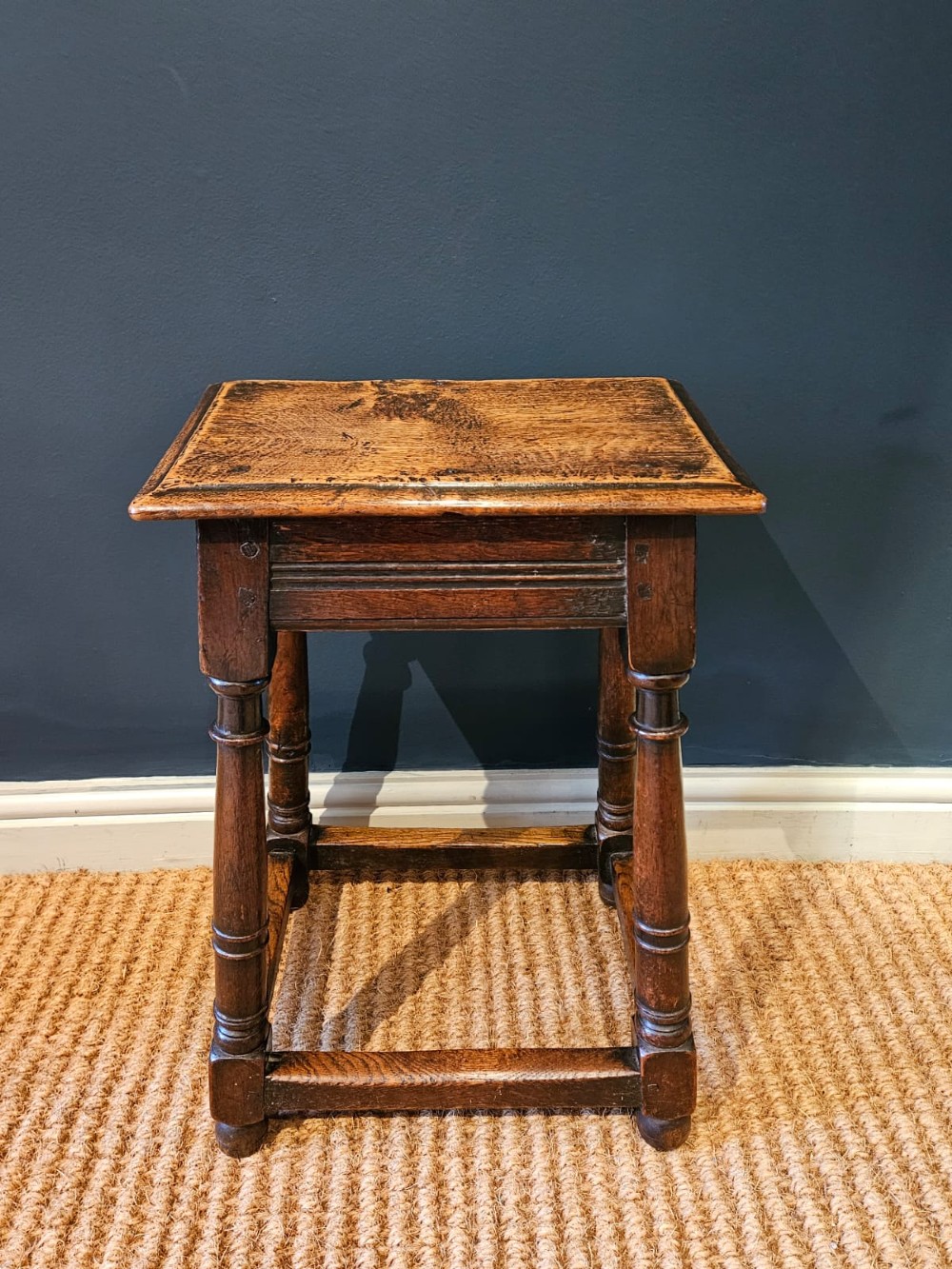 An antique dark oak joint stool featuring a rectangular top, moulded frieze, turned legs, and lower perimeter stretchers. View II