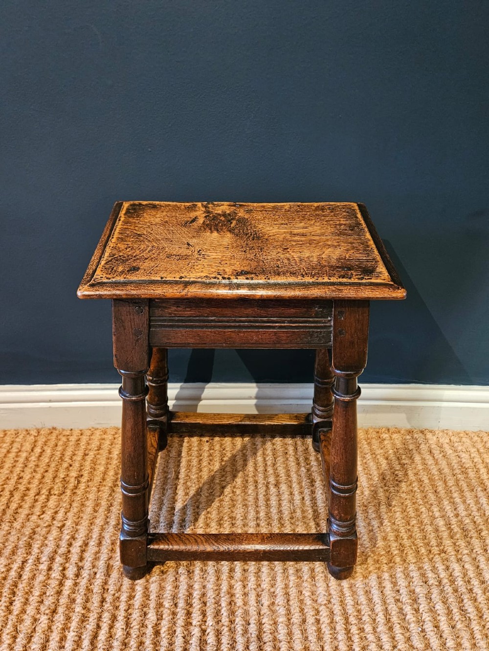 An antique dark oak joint stool featuring a rectangular top, moulded frieze, turned legs, and lower perimeter stretchers. View III