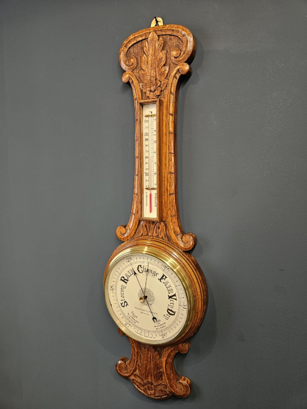 A Victorian carved oak banjo barometer featuring an upper thermometer tube and a lower circular brass-rimmed aneroid dial. View III
