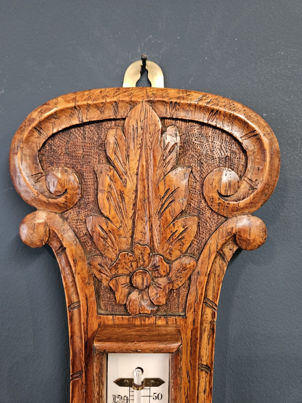 A Victorian carved oak banjo barometer featuring an upper thermometer tube and a lower circular brass-rimmed aneroid dial. View IV