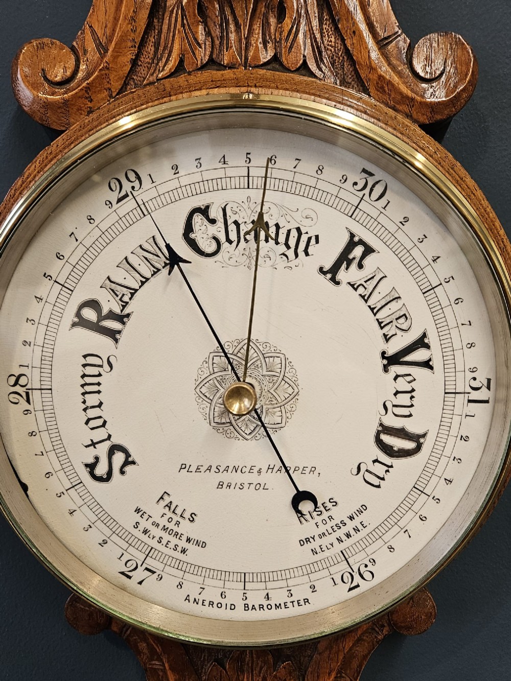 A Victorian carved oak banjo barometer featuring an upper thermometer tube and a lower circular brass-rimmed aneroid dial. View V