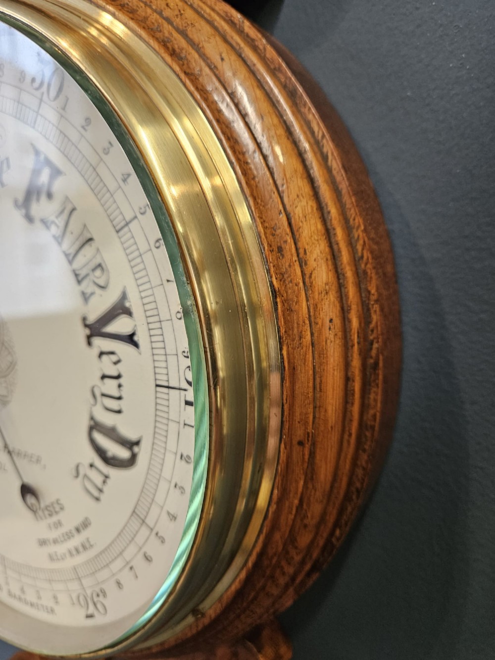 A Victorian carved oak banjo barometer featuring an upper thermometer tube and a lower circular brass-rimmed aneroid dial. View VI